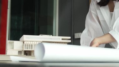 Asyalı genç ve güzel mimar mühendisimiz masaya model konulmuş proje planına bakıyor. Profesyonel proje yöneticisi ev yapısını analiz ediyor. İş tasarımı konsepti. Yönlendirici.