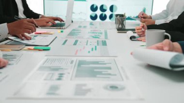 Çeşitli profesyonellerden oluşan bir grup, masalar ve ekranlarda gösterilen mali veri ve grafikleri analiz ederek çağdaş bir ofiste işbirliği yapıyor. İş teması için mükemmel. SACTR
