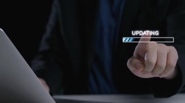 Sistem güncellemesi sırasında dizüstü bilgisayar kullanan birinin yakın plan görüntüsü. Bir dijital yükleme çubuğu ve simgeler, bağlantı ve güvenliği sembolize ederek teknoloji sürecini gösteriyor. Dörtgen