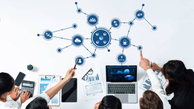 Modern bir ofis alanında dizüstü bilgisayarlar, kağıtlar ve çizelgeler üzerinde takım çalışması, dijital bağlantılar ve veri analizlerinin sergilendiği bir şirket toplantısının tepeden tırnağa görüntüsü. Dostluk