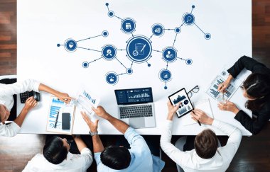 Bir grup dinamik profesyonel, modern ofis ortamında dijital cihazlar kullanarak, verileri analiz ederek ve stratejileri tartışarak, işbirlikçi bir toplantıya girişiyor. Dostluk