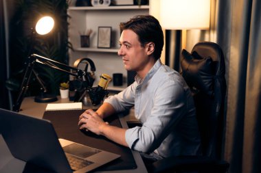 Sunucu kanalı akıllı yayıncı laptopta canlı sosyal medya uygulaması arıyor, kulaklık takıyor ve modern ofis stüdyosundaki mikrofonu kullanıyor. Bireysel.