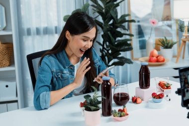 Gülümseyen, güzel Asyalı genç, lezzetli karışık çilek ve kiraz suyu detoksu içeceklerini inceleyen, sosyal medyada özel promosyon satışı için sağlıklı ürünler sergileyen. Taktik.