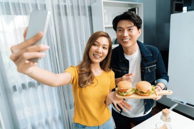 Gülümseyen sunucu şefler akıllı telefonla selfie çekerek sosyal medya kanalından canlı yayında yemek programında çift büyük hamburger yapıyorlar. İnfobahn.