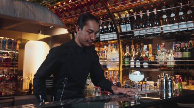 Asyalı barmen karışık kremalı votka bardağı servis ediyor. Önünde buzlu pembe çiçekli şeker, önünde özel içecek, lüks tezgah barında alkolü canlandırıyor. Vinosity.