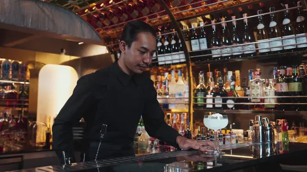 Asyalı barmen karışık kremalı votka bardağı servis ediyor. Önünde buzlu pembe çiçekli şeker, önünde özel içecek, lüks tezgah barında alkolü canlandırıyor. Vinosity.