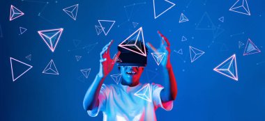 Geometrik şekillerde süzülürken mavi arka planda duran zeki çocuk. Afrikalı bir adam oyun oynuyor, VR gözlük takıyor ve sıradan bir gömlek giyiyor. Gelişmiş gerçeklik teknolojisi yenilik kavramı. Yaratıcılık.