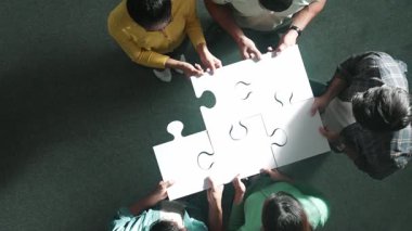 İş dünyasına yukarıdan bakan insanlar bulmacayı tamamlamak için yapbozun son parçalarını bir araya getiriyorlar ve günlük giysiler giyerek ayakta duruyorlar. Çeşitli takımlar takım çalışması ile çözüm buluyor. Sempozyum.