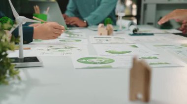 Takım çalışmalarının ve yaratıcılığın yer aldığı canlı bir ofis sahnesi, çizelgeler ve çevre dostu unsurların yer aldığı, sürdürülebilir kalkınma ve yeşil girişimlere odaklanmış. SACTR