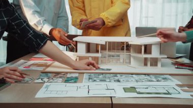 Çeşitli mimarlardan oluşan bir ekip, modern bir ofisteki yeni bir konut projesinde strateji oluşturmak için planlar ve modeller üzerinde çalışan yaratıcı bir toplantıya katılıyor. SACTR