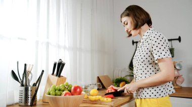 Enerjik anne, mutfak malzemeleri ile çevrili sebzeleri doğrarken modern mutfakta kahvaltı için salata yapıyor. Akıllı kadın temizlikçi yemek pişirir ve yemek hazırlar. Sağlıklı bir yaşam tarzı. Pedagoji.