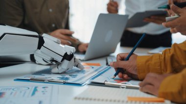 Bir robotik kol modern ofis ortamında bir ekibe yardımcı olur, bir iş analizi sırasında teknoloji ve insan işbirliğinin bir karışımını vurgular. Noogenesis