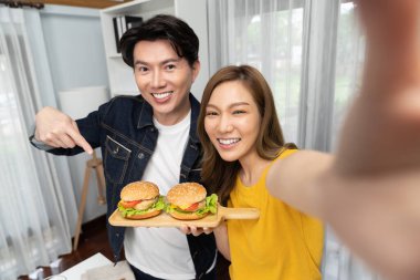 Gülümseyen sunucu şefler akıllı telefonlarıyla fotoğraf çekiyorlar. Özçekim yoluyla. Yemek programında çift hamburger tutuyorlar. İnfobahn.