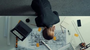 Yetenekli proje yöneticisinin proje planının zaman aşımına uğraması ve toplantı masasında bulunan mimar mühendise ekipman, cetvel, güvenlik kaskı ve dizüstü bilgisayar dağınıklığı ile ev tasarımını açıklamak. Hizalama.