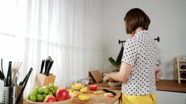 Kafkaseli anne kahvaltıda sebze pişirirken mutlu anne de modern mutfakta salata için taze malzemeler hazırlıyor. Hizmetçi sağlıklı yemek pişiriyor. Dikkat konsepti. Pedagoji.