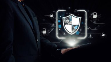 Bir işadamı, siber güvenliği temsil eden dijital kalkan grafiğini gösteren bir tablet tutuyor. Modern unsurlar iş dünyasındaki teknoloji ve güvenliği vurguluyor. Dörtgen
