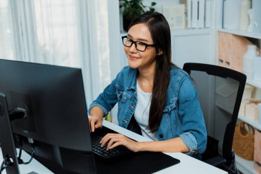 Modern ev ofisinde mavi kot pantolon gömleğiyle sosyal medya planlamasında yeni web sitesi tasarımı ile bilgisayarda arama yapmak için gözlük takan Asyalı genç ve güzel kreatif yönetici üzerinde çalışıyorum. Taktik.