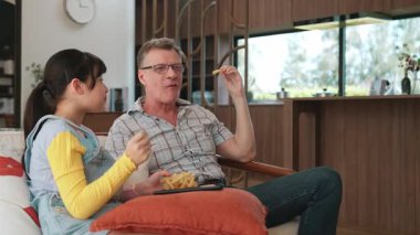 Grandfather and granddaughter eat french fries watch interesting entertainment on TV. Senior use technology communicate with young generation cross generation gap strengthen family bond. Divergence.