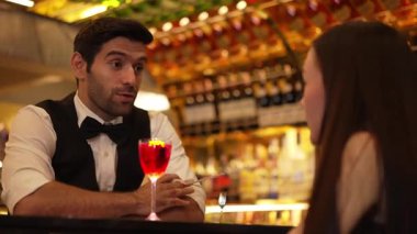 Barmen lüks tezgah barında güzel misafirler için çiçeklerle süslenmiş karışık votka kokteyli servis ediyor. Mükemmel canlı renk sunumu. Atmosfer gece kulübünü ön plana çıkarıyor. Vinosity.