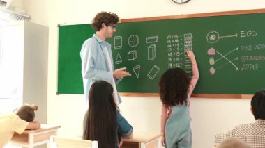 Afrikalı bir öğrencinin tahtada yazarken sorduğu soruya cevap vermesi. Zeki çocuklar matematik dersine katılırken ilkokul öğrencisinin sınıfın önünde matematik sınavı yapmasına bakıyor. Pedagoji.