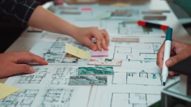 Bir grup profesyonel, modern bir inşaat projesinin tasarım sürecini geliştirmek için renkli notlar ve çizimler kullanarak mimari planlar üzerinde işbirliği yapmaktadır. SACTR