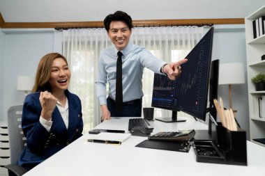 Başarılı gülümseyen Asyalı iş ortakları borsa veritabanında kârlı bir proje için el ele tutuşuyorlar. Yan görüntüdeki modern ev ofisinde resmi takım elbise giyiyorlar. İnfobahn.