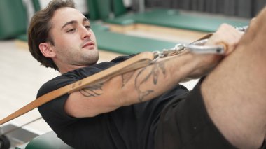 Adam pilates reformatörünü kullanarak çekirdek güçlendirme egzersizi yapıyor. Kolunu ve omzunu güçlendirmek için yüzlerce pozla reformcu üzerinde poz verirken mutlu antrenör pilatesi yakın çekim. Alışkanlık.