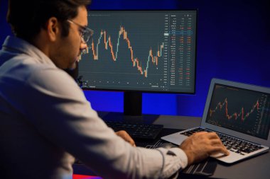 Akıllı tüccar işadamı, karanlık oda gecesinde neon ışıklı ofisteki arama pazarında yüksek kârla ekranda bilgisayar ve bilgisayar üzerinde dinamik borsa yatırımları üzerinde yoğunlaşıyor. Tahmin et..