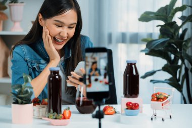 Gülümseyen, güzel Asyalı genç, lezzetli karışık çilek ve kiraz suyu detoksu içeceklerini inceleyen, sosyal medyada özel promosyon satışı için sağlıklı ürünler sergileyen. Taktik.