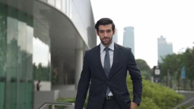 Profesyonel iş adamı hareket ediyor ve kameraya bakarken ayakta duruyor. Gülümseyen yönetici kameraya kendinden emin bir şekilde gülümsüyor. Mimari binada takım elbiseli yatırımcıların yakın çekimi. Sevinçli..