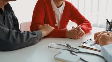 Çift, hastanede jinekoloğun aile planlaması bakımını tarif ederken, koca da genç eşini randevuyla teselli ediyor. Ağır çekim. Katı.