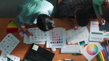 Tasarımcı fikirleri yazarken proje yöneticisinin yukarıdan aşağıya bakan görüntüsü. Akıllı iş adamları logo tasarımı fikrini açıklarken tasarımcılar palete bakarken temayı seçiyorlar. Sempozyum.