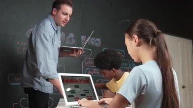 Afrikalı erkek manken tamir ederken beyaz kız programlama ya da kodlama sistemi. Öğretmen elinde dizüstü bilgisayar tutarken çeşitli çocukların web geliştirme programı yazmalarına bakıyor. Yenilik eğitimi. Öğretim