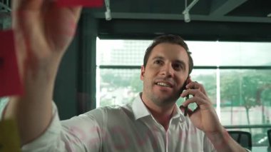 Profesyonel işadamı renkli yapışkan notlara yazılmış pazarlama stratejisi fikrine bakarken müşterilerine telefon ediyor. Proje yöneticisi duvardaki telefon analiz verileriyle konuşuyor. Yönlendirici.