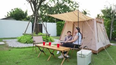 Aile hep birlikte bahçedeki kampta oturup yemek yiyor. Ebeveynler, genç nesil arasında iletişim kurmak ve zaman geçirmek için açık hava kamp faaliyetlerini kullanıyorlar. Uyumsuzluk.