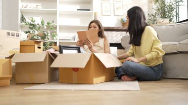 Kutudan kitap seçen ve oturma odasında kitap okuyan mutlu lezbiyen çift. Taşınırken kutular ve mobilyalarla çevrili otururken çekici bir kız konuşuyor ve paketleri açıyor. Yer değiştirin. Myrmidon.