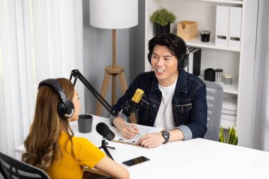 Gülümseyen radyo etkili sunucusu kulaklık takıyor kadın konuşmacı ile röportaj yapıyor sosyal medya internet sitesinden dinleyicilere bilgi paylaşıyor stüdyo kaydında sabah canlı yayın kanalı. İnfobahn.