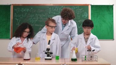 Kafkasyalı zeki öğretmen, meraklı öğrencilerin laboratuardaki deney kabına renkli sıvı dökmesini destekler. Yaratıcı çocuklar deney yapmaya ve biyokimyasal örnekleri incelemeye konsantre olurlar. Pedagoji.