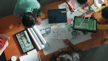 Yetenekli iş adamlarının tablet tutması ve planlara bakması. Masada dizüstü bilgisayarla dururken mimarın tasarım ve planlama bölümünün havadan görüntüsü. Sempozyum.