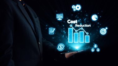 Bir işadamı, dijital simgelerle çevrili bir maliyet azaltma grafiğini gösteren, mali stratejileri, yeniliği ve iş verimliliğini sembolize eden bir tablet tutuyor. Dörtgen