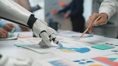 Bir robot el, modern bir ofiste veri grafiklerini ve grafiklerini analiz etmek için insan eliyle işbirliği yapar. İş dünyasındaki teknoloji ve takım çalışmasının karışımını açıklar. Noogenesis