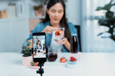 Seçici odaklı akıllı telefon ve gülümseyen genç, güzel Asyalı karışık çilek ve kiraz suyu detoksu değerlendirmesi sosyal medyada sağlıklı ürün tanıtımı sunuyor. Taktik.