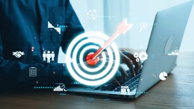 Bu resim, profesyonel bir ortamda iş büyümesini, analitiği ve stratejik planlamayı sembolize eden bir dizüstü bilgisayar ve dijital hedef simgelerinin yer aldığı modern bir çalışma alanını gösteriyor. Dörtgen