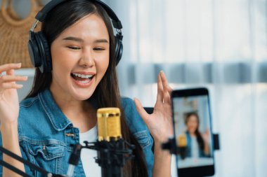 Asyalı sunucu canlı yayında canlı yayında canlı yayında sosyal medyada kulaklık takarak konuşuyor. Dinleyicileri modern stüdyoda koçluk yaparak selamlıyor. Taktik.