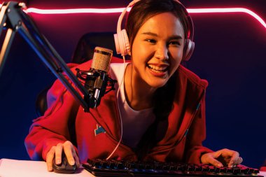 İnternet üzerinden kulaklık takıp gülümseyen Asyalı güzel kız flamasının sunucu kanalı izleyicilerle internet üzerinden konuşma yapıyor. Esport yetenekli takım oyuncuları neon mavi odada. Taktik.