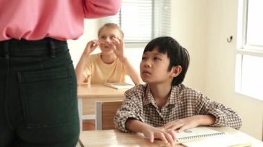 Asyalı ilkokul öğrencisi sınıfta öğretmenine bakıyor. Sınıfta oturan çeşitli zeki öğrenciler, öğretmenleri sınıf çalışmalarını ve sınavlarını anlatırken. Eğitim konsepti. Pedagoji.