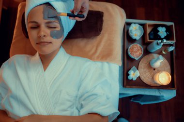 Kaplıca salonunun sakin atmosferi, üst düzey kadın müşteri sıcak mum ışığında kömür kömürü yüz kremi masajıyla kendini yenilemeye çalışıyor. Yüz bakımı ve güzellik konsepti. Sessiz.