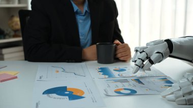 Bir iş adamı modern bir masada oturur, çizelge ve grafikleri robot koluyla analiz eder, teknolojiyle insan öngörüsünü gelecekteki ofis ortamında birleştirir. Noogenesis