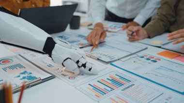 Bir robot el, verimli bir toplantı sırasında çizelge ve grafikleri analiz eden bir iş ekibiyle birlikte çalışır ve teknolojinin iş yerinde bütünleşmesini vurgular. Noogenesis