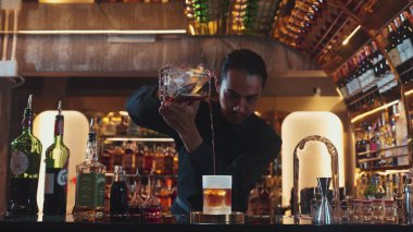 Asyalı barmen soğuk bardağa karışık viski dökerek soğutmalı buzlu içecek üretiyor. Lüks ılık barlarda alkol yenileme gösterisine odaklanan yaratıcı bir reklam yapıyor. Vinosity.